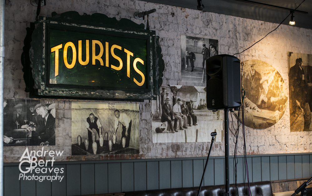 the wall of a pub with old photos of people playing skittles and a light up sign the says tourists