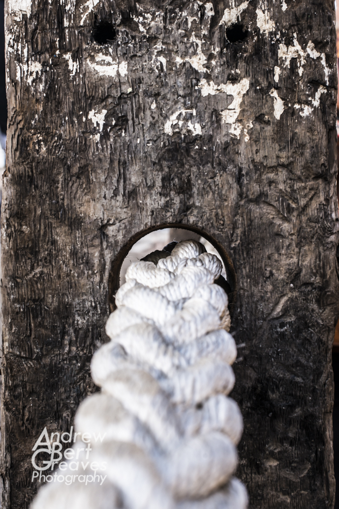 rope through a hole on a wooden post with two holes above that looks like a shocked face